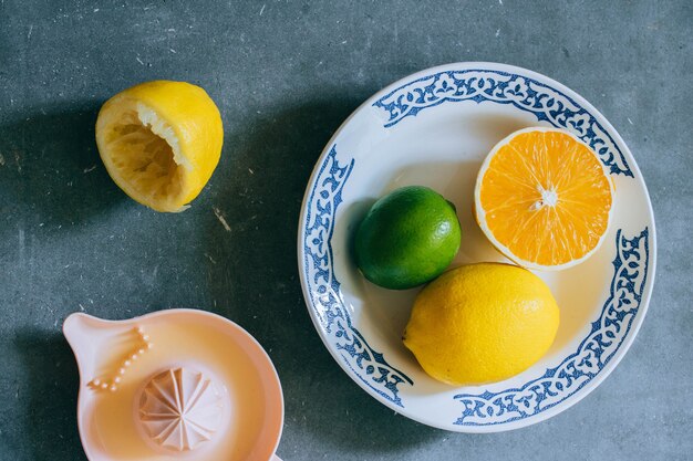 Citrons, citron vert, orange dans une assiette en céramique blanche avec un motif, presse-agrumes