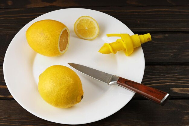 Citrons sur couteau à assiette blanche et pulvérisateur de jus frais sur une surface en bois