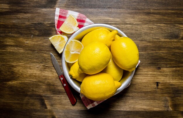 Les citrons dans la tasse avec un couteau sur le tissu. Sur une table en bois. Vue de dessus