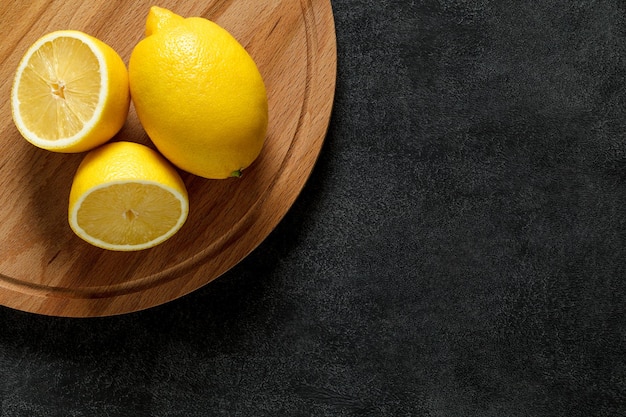 Citrons entiers et coupés sur une planche à découper en bois ronde sur fond sombre vue de dessus espace pour copier du texte