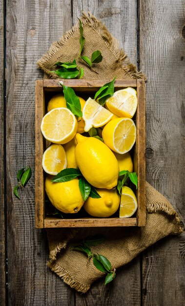 Citrons avec des feuilles dans une boîte sur le tissu sur une table en bois. Vue de dessus