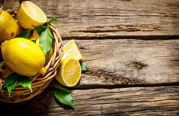 Citrons frais dans un panier avec des feuilles. Sur fond en bois. Espace libre pour le texte. Vue de dessus