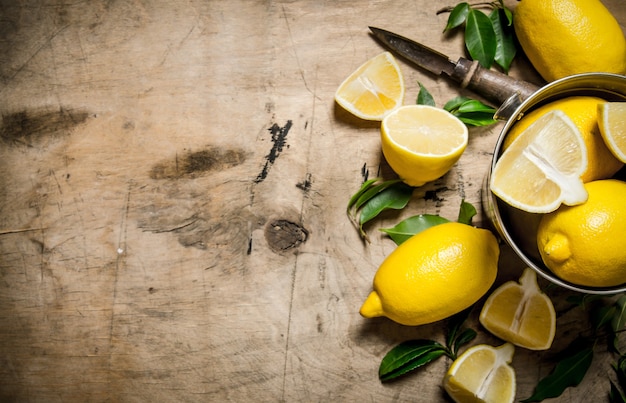 Citrons frais dans un seau de feuilles. Sur table en bois.