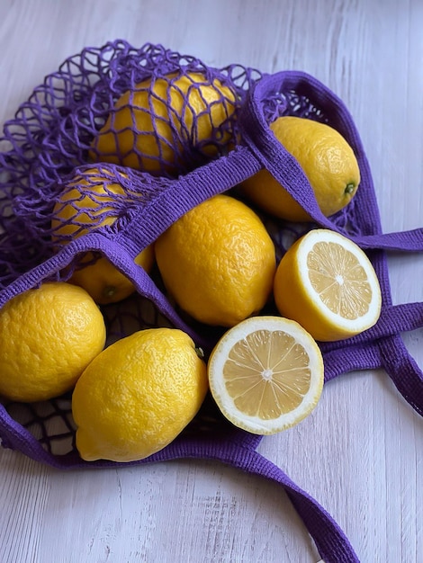 citrons jaunes dans un sac à cordes violet, citrons sur fond de bois gris, place pour le texte