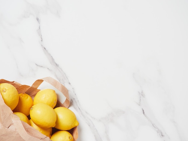 Citrons jaunes dans un sac en papier placé dans le coin inférieur gauche sur le comptoir en marbre comme arrière-plan, vue de dessus avec espace de copie.