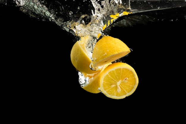 Des citrons jaunes frais dans de l'eau éclaboussée sur un fond noir