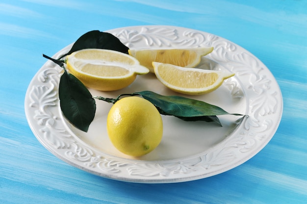 Citrons jaunes frais avec des feuilles sur une assiette sur fond bleu