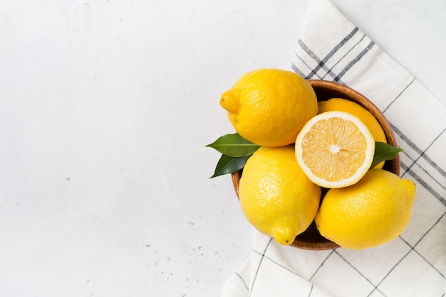 Citrons mûrs dans un bol avec des feuilles sur blanc. vue de dessus