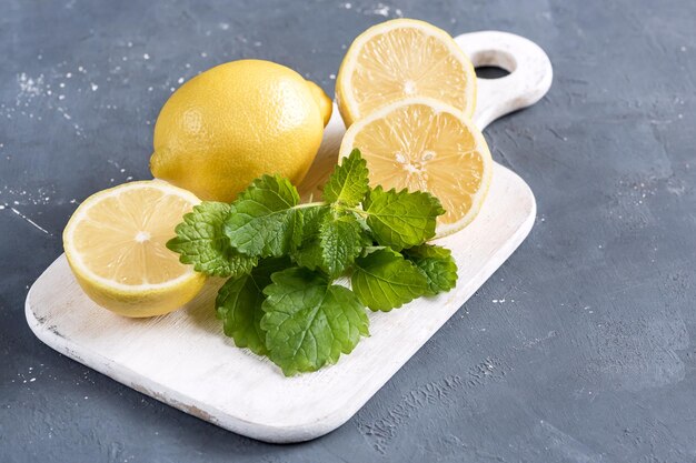 Citrons sur une planche à découper sur fond gris Feuille de menthe jaune fraîche d'agrumes