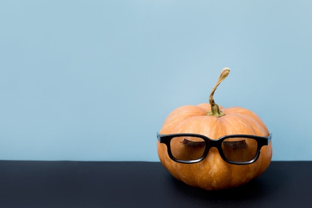 Citrouille avec faux cils et lunettes de soleil sur fond bleu, Halloween