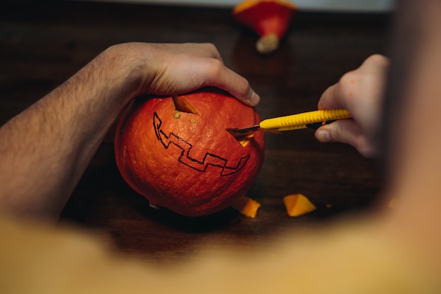 Citrouille d'Halloween de Jack. Les mains de l'homme découpant la bouche avec un coupe-papier. Image avec mise au point sélective. photo de haute qualité