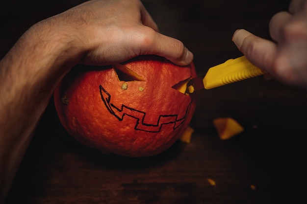 Citrouille d'Halloween de Jack. Les mains de l'homme découpant la bouche avec un coupe-papier. Image avec mise au point sélective. photo de haute qualité