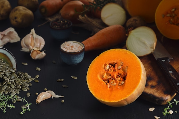 Citrouille jaune mûre coupée en deux pour faire une soupe à la crème de saison. Gros plan, mise au point sélective sur la citrouille. Ingrédients, légumes et épices pour faire de la soupe à la citrouille sur une table en bois noir