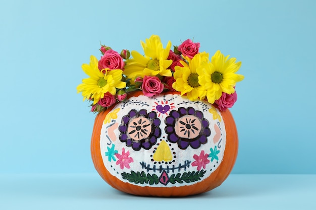 Citrouille avec maquillage de crâne de catrina et fleurs sur mur bleu