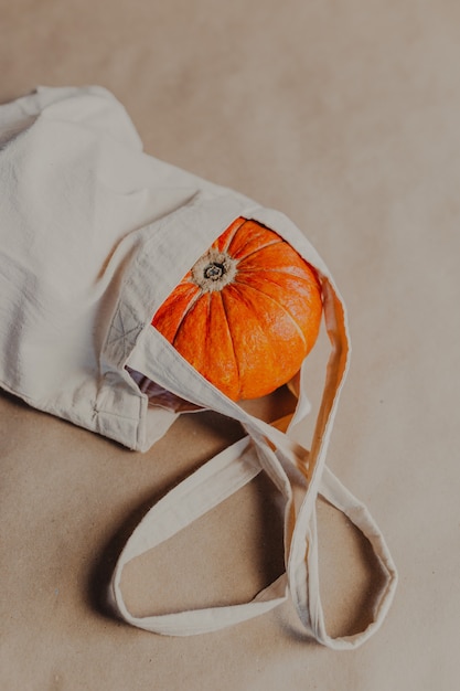 Citrouille orange en beige shopper sur fond de papier. Citrouille d'Halloween à l'intérieur du sac beige.