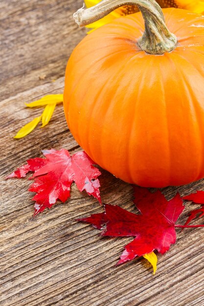 Une citrouille orange avec des feuilles d'automne sur une table texturée en bois