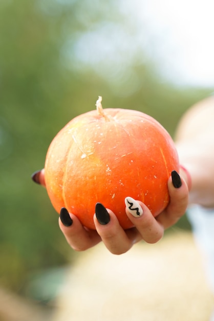 Photo citrouille orange sur une paume femelle avec manucure noire sur les ongles