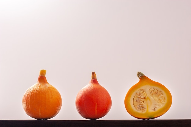 Une citrouille rouge, une jaune et une coupée avec des graines à l'intérieur, sont alignées sur un fond blanc. Citrouille rouge au centre. Espace de copie.