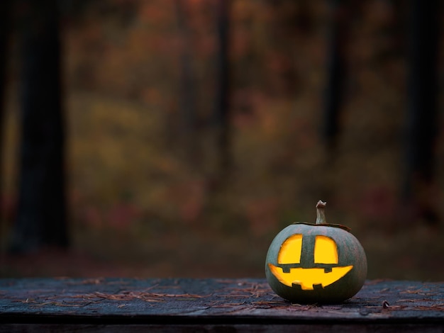 Citrouille rougeoyante sculptée sur une table en bois dans la forêt d'automne pour l'espace de copie d'Halloween