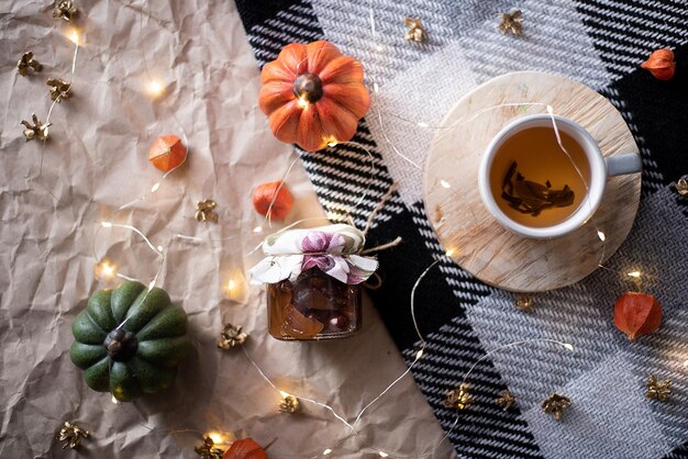 Citrouille avec une tasse de thé sur un plaid à carreaux pot de confiture décor d'automne mise à plat