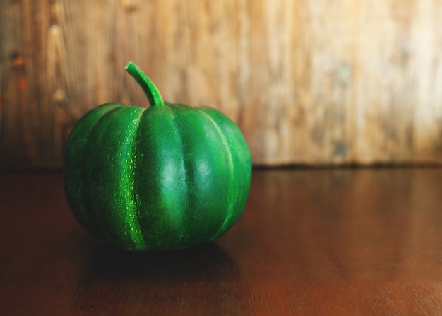 Citrouille verte avec tige sur table en bois foncé.