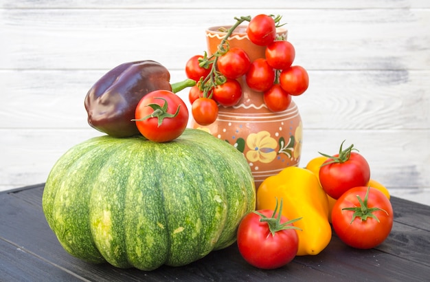 Citrouille verte, tomates, poivre et cruche sur fond noir en bois