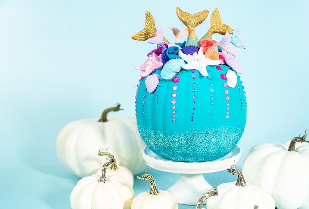 Citrouilles artisanales d'Halloween décorées de queues de sirène, de paillettes et de strass scintillants sur fond bleu.