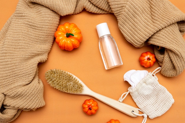 Des citrouilles, une brosse naturelle pour le corps, un démaquillant, des éponges et un pull chaud sur fond beige. Cosmétiques pour le visage et le corps. Mise en page d'automne. Vue de dessus