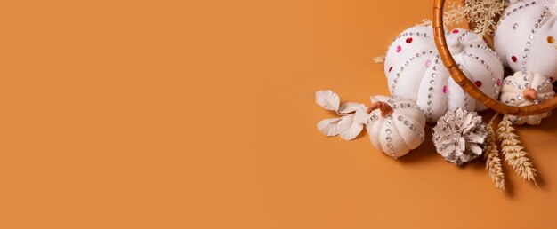 Citrouilles décoratives blanches faites à la main avec des pierres brillantes et des pommes de pin dans le panier sur fond coloré Concept de récolte d'automne