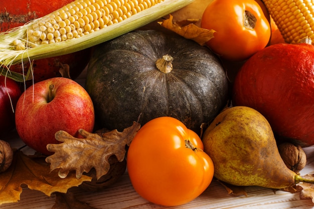 Citrouilles de différents légumes, pommes, poires, noix, maïs, tomates, feuilles jaunes sèches sur fond en bois blanc. Récolte d'automne, surface.