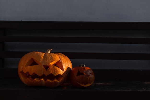 Citrouilles d'Halloween effrayantes debout sur un banc de jardin près d'un mur le soir