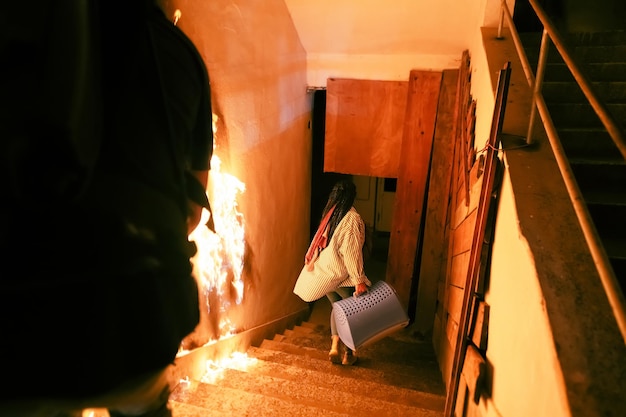 Un civil courageux transportant un bébé et un animal de compagnie chat ou chien dans une boîte ou un sac, descend les escaliers d'un bâtiment en feu. Ouvrez le feu et un pompier en arrière-plan. Photo de haute qualité