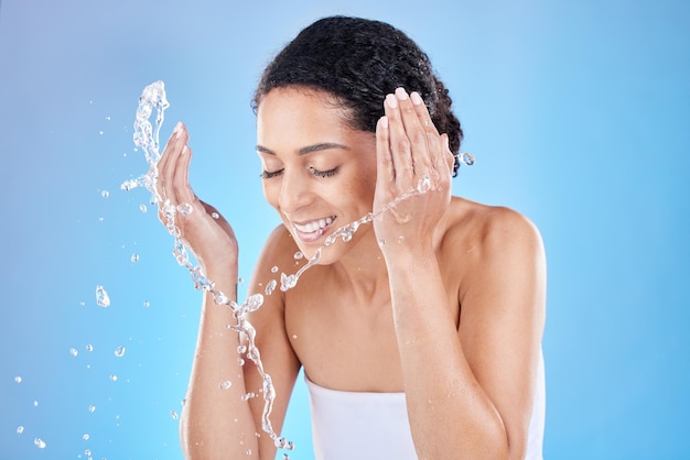 Éclaboussure d'eau de femme noire pour le nettoyage du visage soins de la peau bien-être ou spa de luxe beauté du visage en studio sur fond bleu Sourire de la peau ou modèle de fille heureuse pour la publicité de douche d'eau ou de cosmétiques de santé