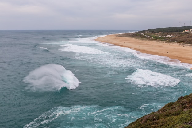 Éclaboussure de vagues dans le vent sur les rives de Nazare.