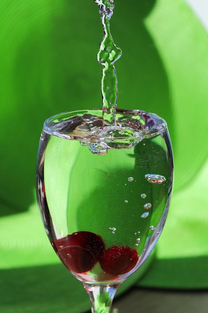 Éclaboussures dans un verre avec de l'eau et des baies sur un fond vert clair.