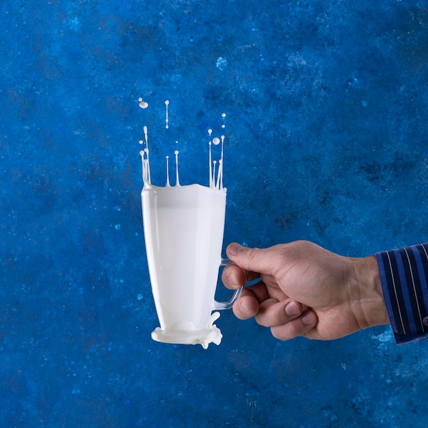 Éclaboussures de lait dans une lévitation de verre sur fond bleu avec une main