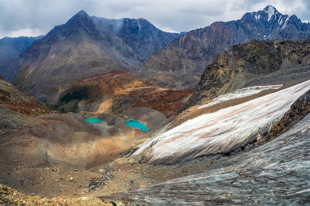 Photo clair-obscur montagnard. impressionnant paysage de montagne sombre avec une énorme montagne enneigée et un glacier illuminé par le soleil parmi de hauts rochers. superbe paysage alpin avec un grand glacier et des lacs.