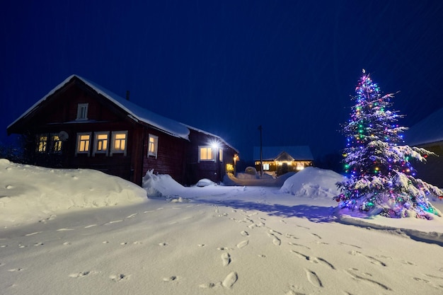 Éclairage électrique dans les fenêtres d'une maison de campagne dans un village de nuit enneigée la veille de Noël dans le nord