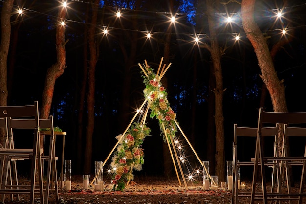 Éclairage de guirlandes de fête sur un décor d'arc de tipi bohème sur le lieu de la cérémonie de mariage en plein air en pin