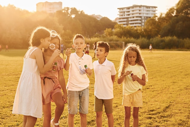 Éclairé par la lumière du soleil Debout sur le terrain de sport Un groupe d'enfants heureux est à l'extérieur pendant la journée