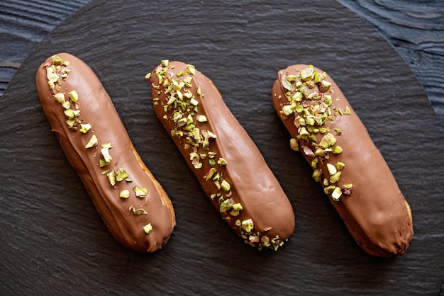 Éclairs ou profiteroles avec glaçage au chocolat au lait et pistaches sur plaque de pierre noire se bouchent