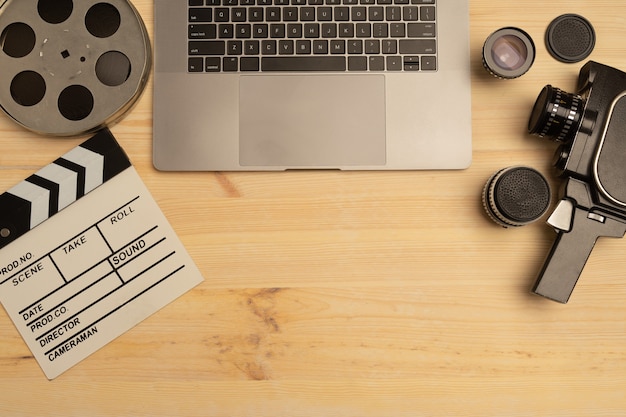 Clap de cinéma, ordinateur portable et appareil photo sur table en bois, vue de dessus