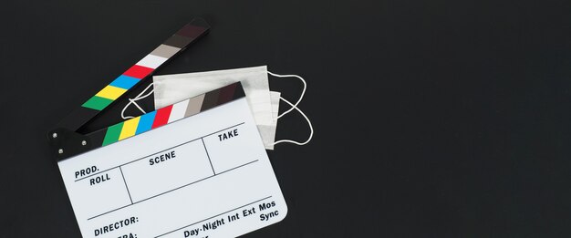 Clapper board ou ardoise de film et masque facial, mégaphone sur fond noir. Il est utilisé dans la production vidéo et l'industrie cinématographique.