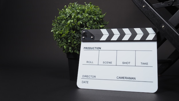 Clapperboard ou clap board ou ardoise de film avec chaise de réalisateur utilisée dans la production vidéo, le cinéma, l'industrie du cinéma sur fond noir.