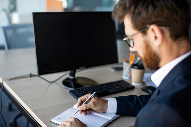 Classe affaires en ligne Employé de bureau masculin écrivant dans un cahier prenant des notes et utilisant un ordinateur avec une maquette d'écran noir