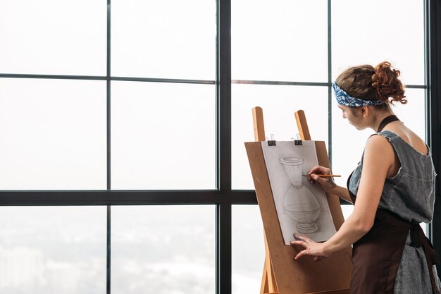 Classe d'art plastique. Vue latérale du croquis de dessin de jeune femme de vase en studio