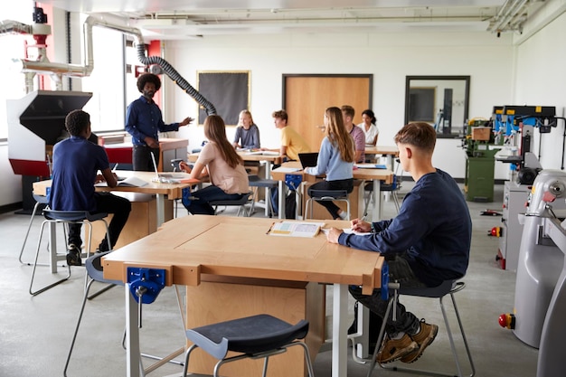 Classe d'élèves du secondaire assis sur des bancs de travail à l'écoute de l'enseignant dans la leçon de conception et de technologie