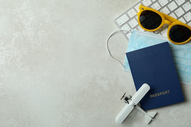 Clavier, avion jouet, passeport, lunettes de soleil et masque médical sur fond texturé blanc