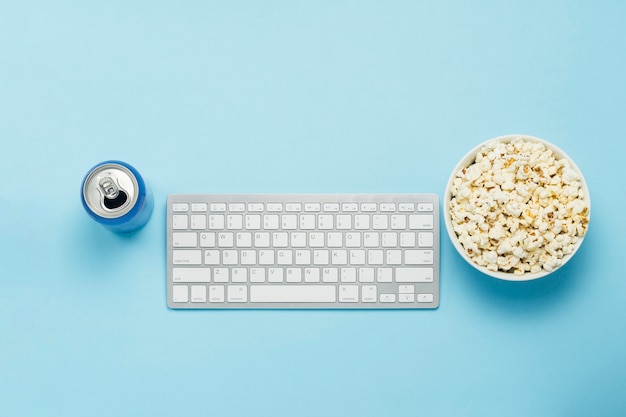 Clavier et boîte de conserve avec une boisson, une boisson énergisante, un bol de pop-corn sur fond bleu. Le concept de regarder des films, des émissions de télévision, des événements sportifs en ligne. Mise à plat, vue de dessus