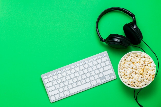 Clavier, casque et un bol de pop-corn sur fond vert. Le concept de regarder des films, des émissions, des sports sur PS, des jeux en ligne. Mise à plat, vue de dessus.